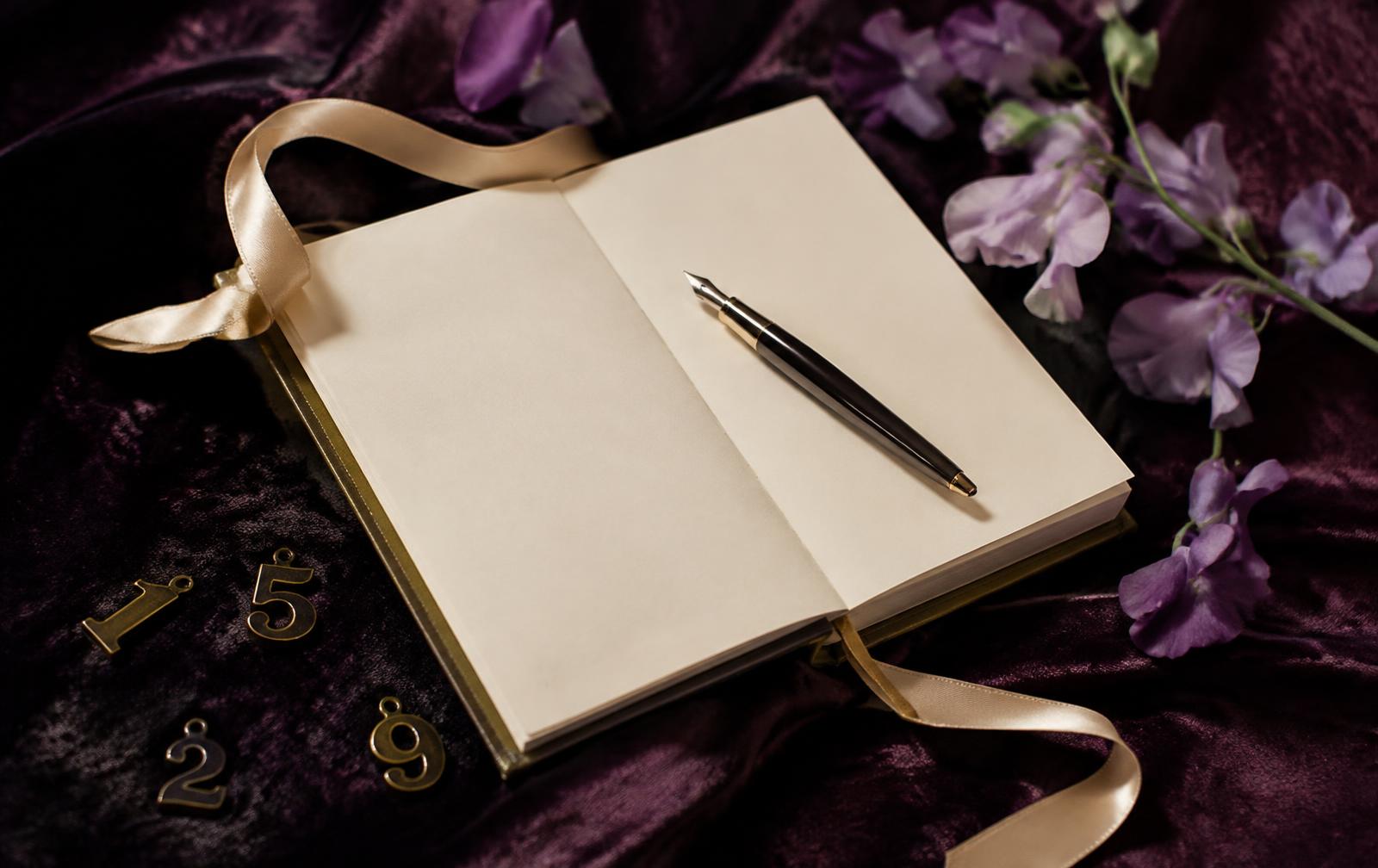 An open ivory notebook with a fountain pen, brass numerals and lilac sweet peas on plum velvet